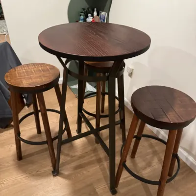 Rustic pub-height table with a dark wood top and dark metal base, accompanied by three matching wooden barstools with circular seats and...