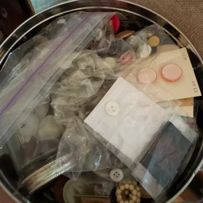 Vintage sewing notions collection, featuring an assortment of buttons on cards and loose in plastic bags, stored inside a round metal tin.