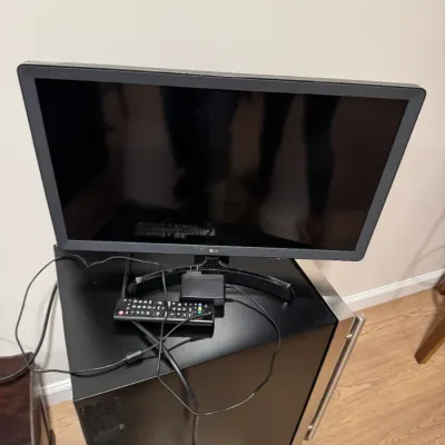 Sale Photo Thumbnail #133: LG flat-screen television monitor with stand, remote control, and power adapter, resting on a black mini-fridge.