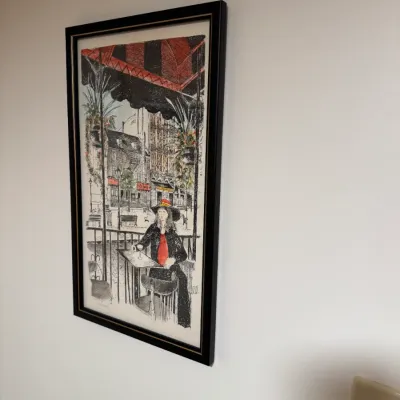 Sale Photo Thumbnail #111: Framed art print depicting a woman seated at an outdoor cafe, rendered in a sketch style with red accents and housed in a black frame.