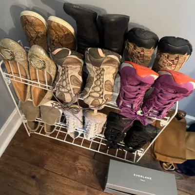 Assorted women's shoes, including athletic sneakers, flats, and boots, displayed on a white wire shoe rack alongside an Everlane...