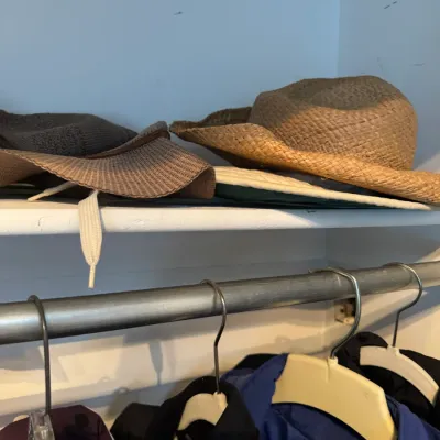 Sale Photo Thumbnail #219: Assorted sun hats and straw hats resting on a closet shelf above hanging garments.