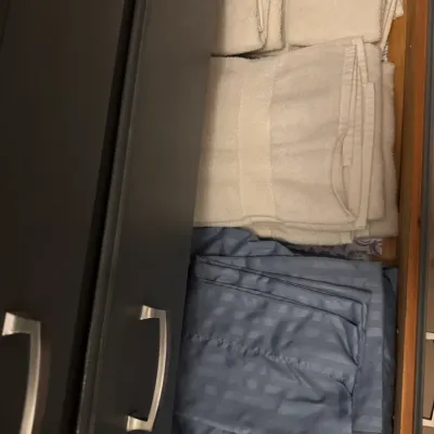 Sale Photo Thumbnail #185: Assorted household linens, including folded white bath towels, hand towels, and a set of blue striped bed sheets, stored inside a dark grey dresser drawer.
