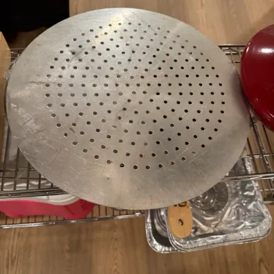 Perforated aluminum pizza pan with a wooden handle, showing some surface wear and scratches from use.