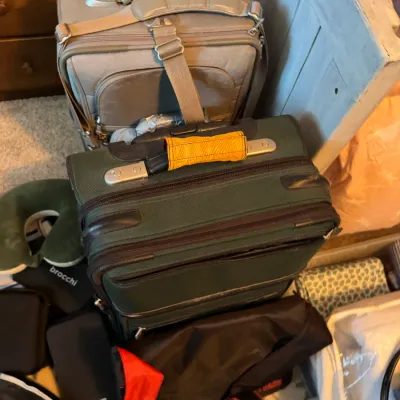 Sale Photo Thumbnail #168: Two soft-sided rolling suitcases, one in grey and one in dark green, shown with travel accessories including a neck pillow and small bags.