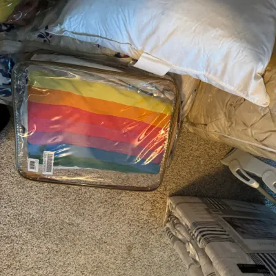 Sale Photo Thumbnail #188: Assorted bedding items, including a rainbow-striped blanket in a clear zippered storage bag, a white pillow, and a packaged twin XL comforter set.