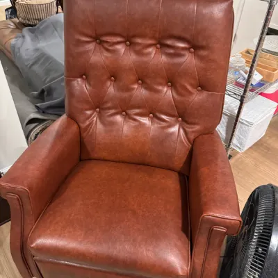 Vintage tufted faux-leather recliner in a warm cognac brown, featuring a high back and rolled arms.