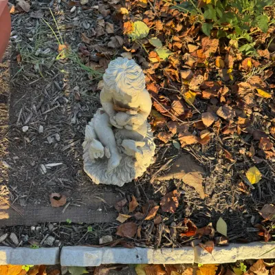Cast stone garden statue depicting a young child cradling a small animal, showing natural weathering and outdoor patina.