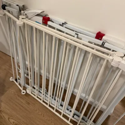 Sale Photo Thumbnail #105: White metal expandable safety gate with vertical bars and red locking mechanisms, suitable for children or pets.
