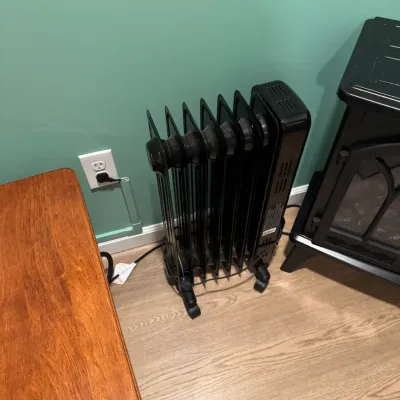 Sale Photo Thumbnail #114: Modern black oil-filled radiator space heater on wheels, shown plugged into a wall outlet.