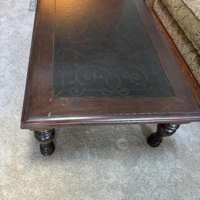 Traditional dark wood coffee table featuring a glass top insert with an elegant scrollwork design and turned baluster legs.