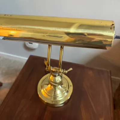 Sale Photo Thumbnail #258: Vintage brass piano or desk lamp with an adjustable arm and cylindrical shade, showing some light surface wear.