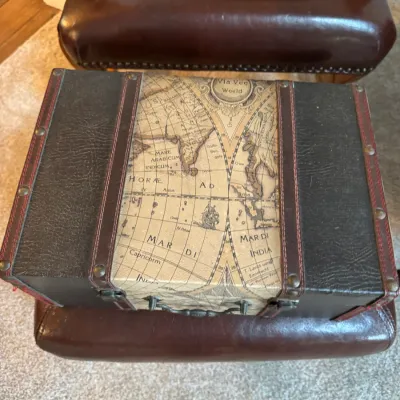 Vintage-style decorative storage trunk featuring a central old-world map design, dark faux-leather trim with red stitching, and...