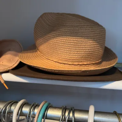 Sale Photo Thumbnail #220: Woven straw fedora hat resting on a closet shelf above a clothing rack.