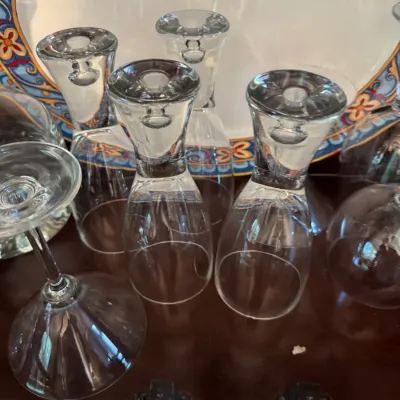 Collection of clear glass stemware, including wine and martini glasses, displayed upside down in front of a decorative ceramic platter.