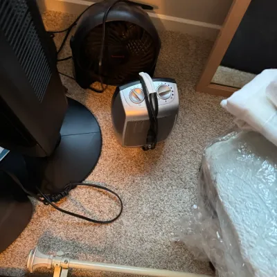Sale Photo Thumbnail #140: Assorted household items including a Honeywell circular fan, a small silver space heater, a tower fan, and curtain rods on a carpeted floor.