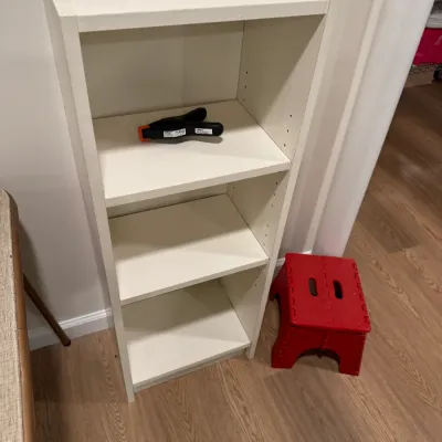 Sale Photo Thumbnail #277: White laminate three-shelf bookcase with adjustable shelves, shown alongside a small red folding plastic step stool.