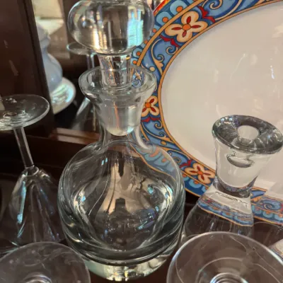 Vintage clear glass decanter with a rounded stopper, displayed alongside glassware and a decorative ceramic plate.