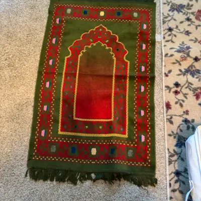 Islamic prayer rug featuring a green and red mihrab design with floral borders and fringed ends.