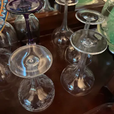 Sale Photo Thumbnail #245: Assorted vintage crystal and glass stemware, including etched floral patterns and a purple-stemmed glass, displayed upside down on a wooden surface.