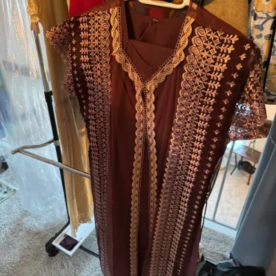 Maroon kaftan-style dress featuring intricate gold embroidery along the front opening and shoulders, displayed on a clothing rack.