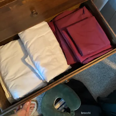 Sale Photo Thumbnail #147: Assorted folded bed sheets in white and burgundy, stored inside a wooden dresser drawer.
