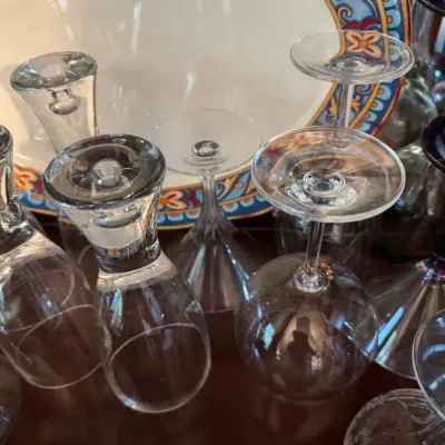 Assorted clear glassware, including wine glasses and tumblers, displayed upside down in front of a decorative ceramic platter with a...