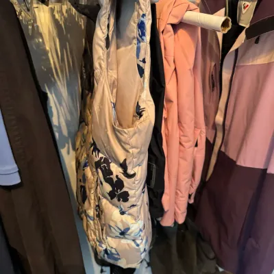 Sale Photo Thumbnail #218: Assorted outerwear hanging in a closet, including a floral print puffer vest, a pink jacket, and a Rossignol ski jacket.