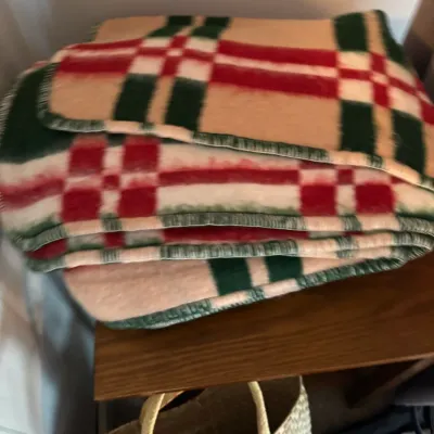 Sale Photo Thumbnail #162: Vintage wool camp blanket featuring a red, green, and cream plaid pattern, folded on a wooden shelf.