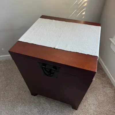 Contemporary dark wood storage trunk or side table with a hinged lid, black metal latch, and a light grey fabric runner.