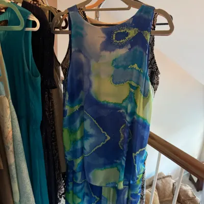 Sale Photo Thumbnail #157: Sleeveless watercolor-print dress in shades of blue, green, and yellow, hanging on a clothing rack alongside other garments.