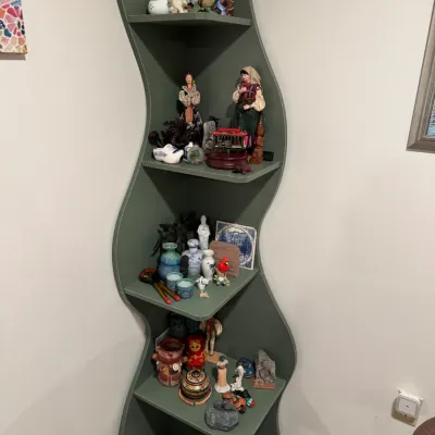 Sale Photo Thumbnail #280: Modern sage green corner shelving unit with wavy, organic-shaped sides, displaying various small collectibles and figurines.
