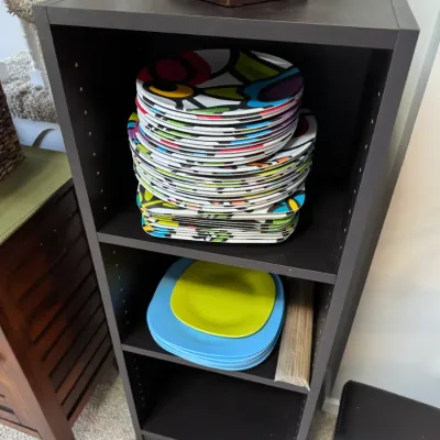 Sale Photo Thumbnail #264: Dark brown laminate three-shelf bookcase holding stacks of colorful, modern melamine plates.