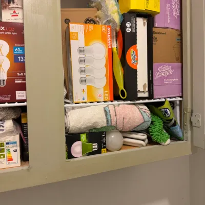 Sale Photo Thumbnail #234: Assorted household cleaning supplies and light bulbs, including Swiffer refills, Sylvania LED bulbs, and microfiber cloths, organized inside a utility cabinet.