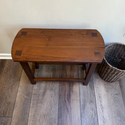 Mission-style wooden bench with exposed joinery details on the seat, shown alongside a woven basket on laminate flooring.