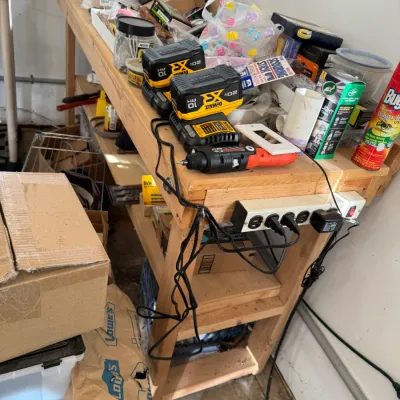 Sale Photo Thumbnail #214: DeWalt 20V Max lithium-ion batteries and charger sitting on a wooden workbench cluttered with various tools, hardware, and household items.