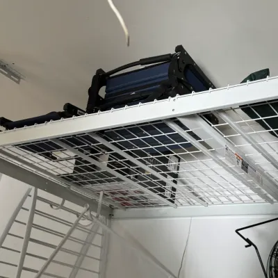 Sale Photo Thumbnail #205: White wire overhead garage storage rack holding folded blue camping chairs and other items.