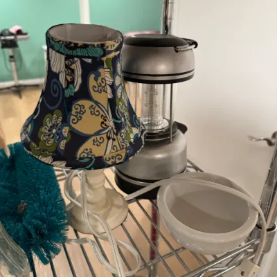 Small accent lamp with a blue and yellow floral fabric shade, shown alongside a silver camping lantern and a white ceramic bowl on a wire...