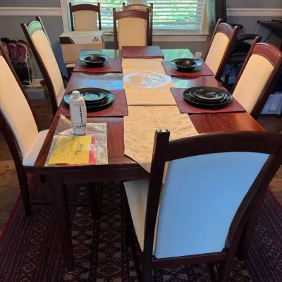 Contemporary cherry-finished dining table with six matching high-back chairs featuring cream-colored upholstered seats and backrests.