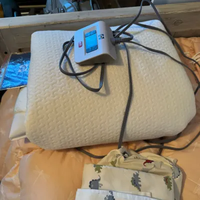Sale Photo Thumbnail #166: ChiliPad sleep system control unit and mattress pad, shown with power cords and folded dinosaur-patterned sheets.