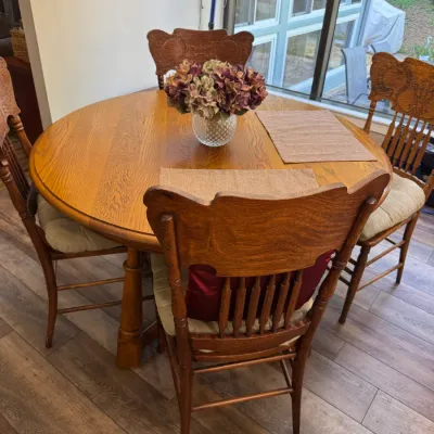 Vintage oak dining set featuring a round pedestal table and four pressed-back chairs with spindle details and upholstered seat cushions.