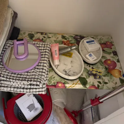 Sale Photo Thumbnail #120: Assorted bathroom accessories and cleaning supplies, including a purple hand mirror, marble-patterned trays, towels, and a spin mop bucket.