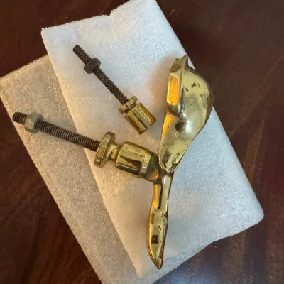 Vintage polished brass hardware piece, possibly a door knocker or handle component, shown with mounting screws and nuts on protective foam.
