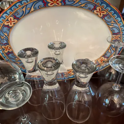 Large oval ceramic serving platter with a colorful Mediterranean-style border, displayed behind a collection of clear glass stemware.