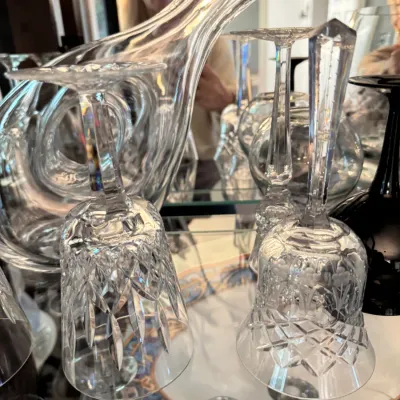 Assorted crystal glassware, including a cut crystal bell, wine glasses, and a modern glass decanter, displayed on a mirrored shelf.