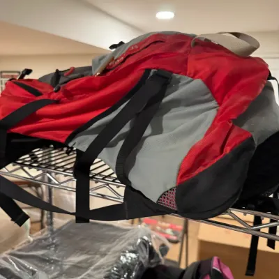 Red and gray nylon hiking backpack with black straps, resting on a wire storage shelf.