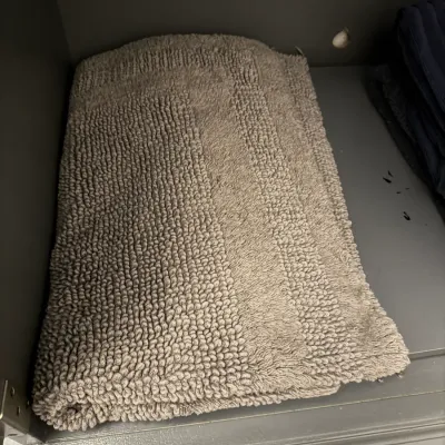 Sale Photo Thumbnail #181: Folded grey cotton bath mat with a textured loop pile, stored on a shelf.