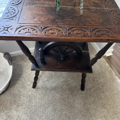 Vintage dark-stained oak side table featuring a carved floral border on the tabletop, turned legs, and a lower shelf with a decorative...