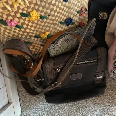 Sale Photo Thumbnail #159: Assortment of handbags including a brown Tumi nylon messenger bag, a woven straw tote with floral embroidery, and a patterned fabric purse.