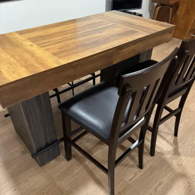 Modern counter-height dining table with a wood-grain top and dark gray pedestal base, accompanied by two matching dark wood barstools...